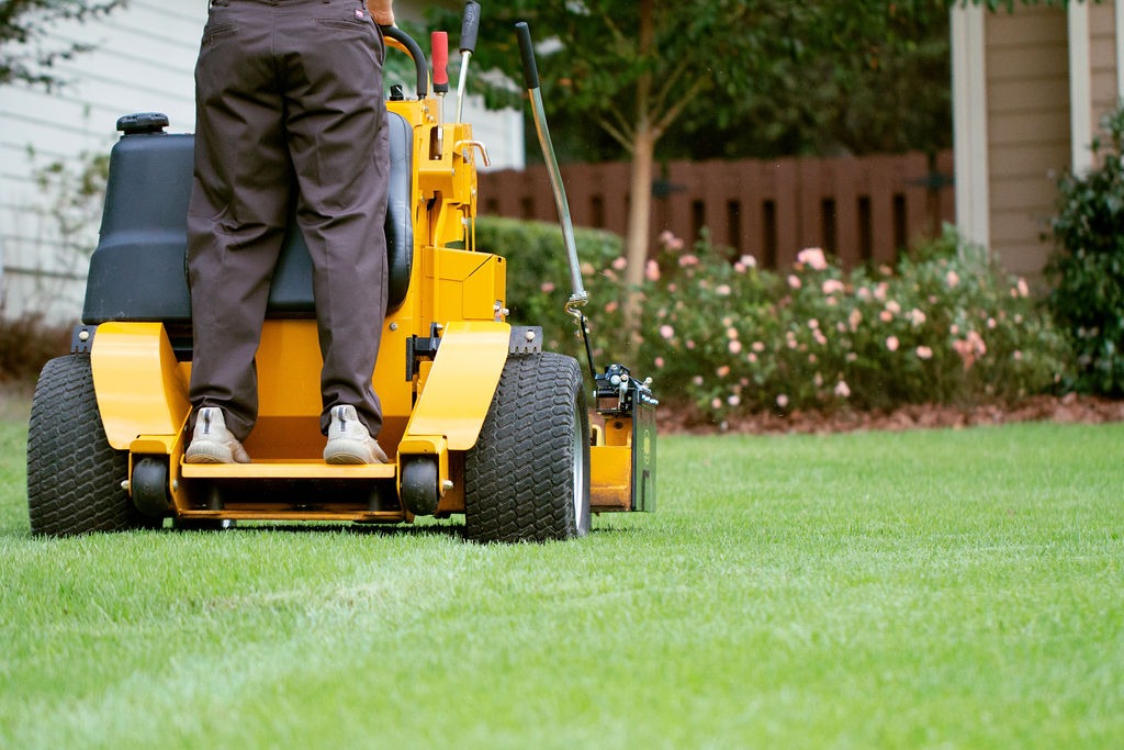 Landscaper operating yellow stand-on mower across residential lawn