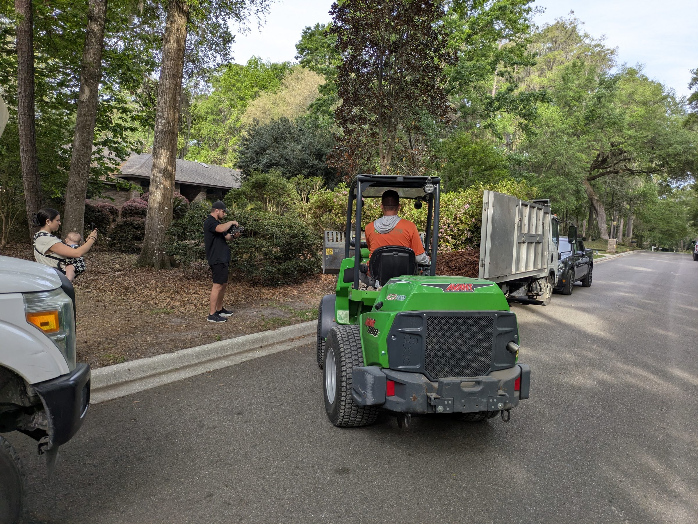 Landscaping crew works beside truck on tree-lined residential street