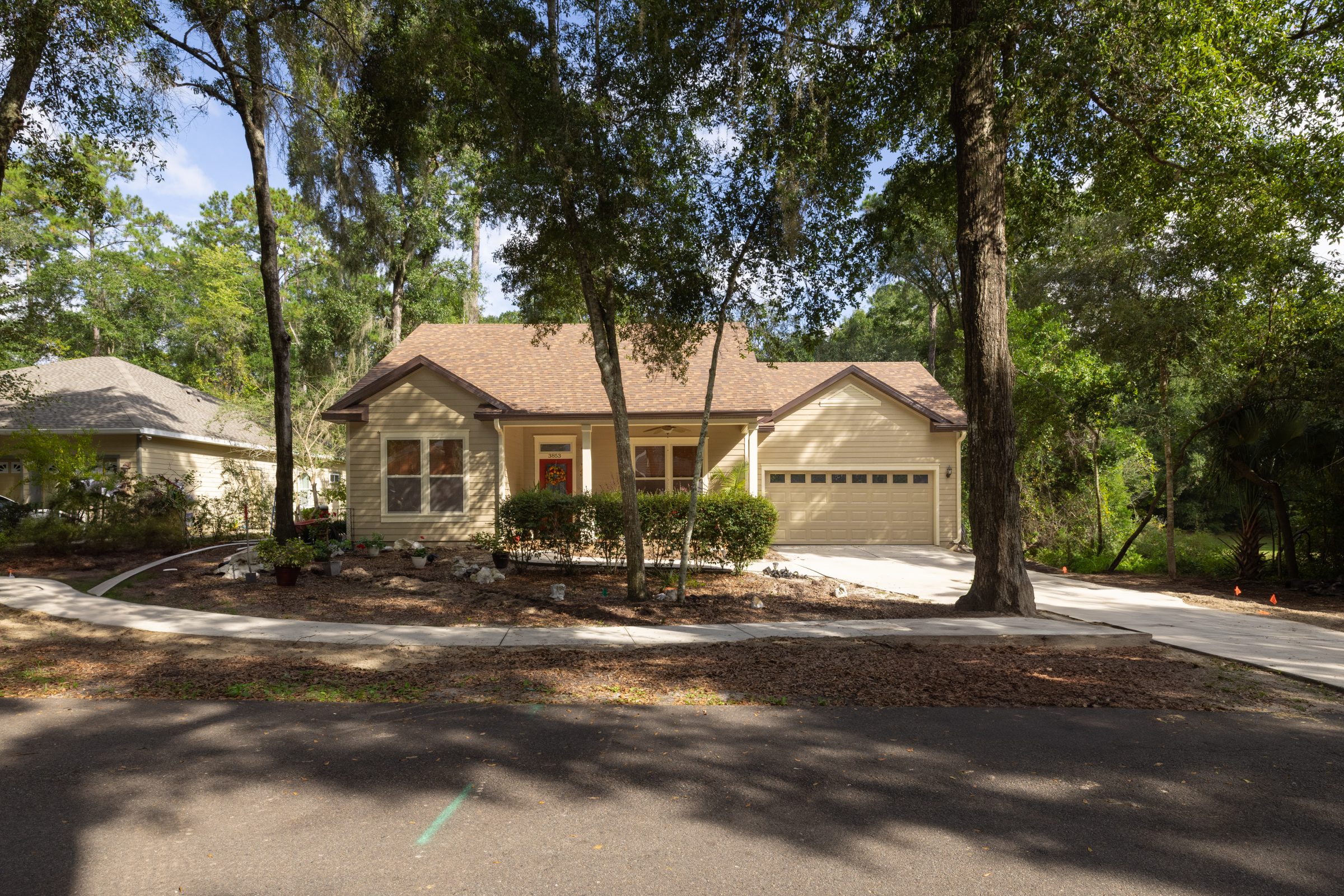 Beige single-story home with garage beneath mature trees