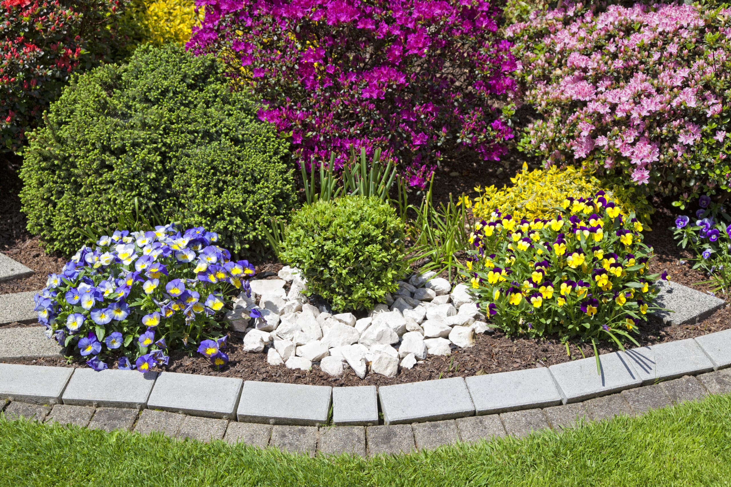 A gorgeous arrangement of flower bushes with a stone border.