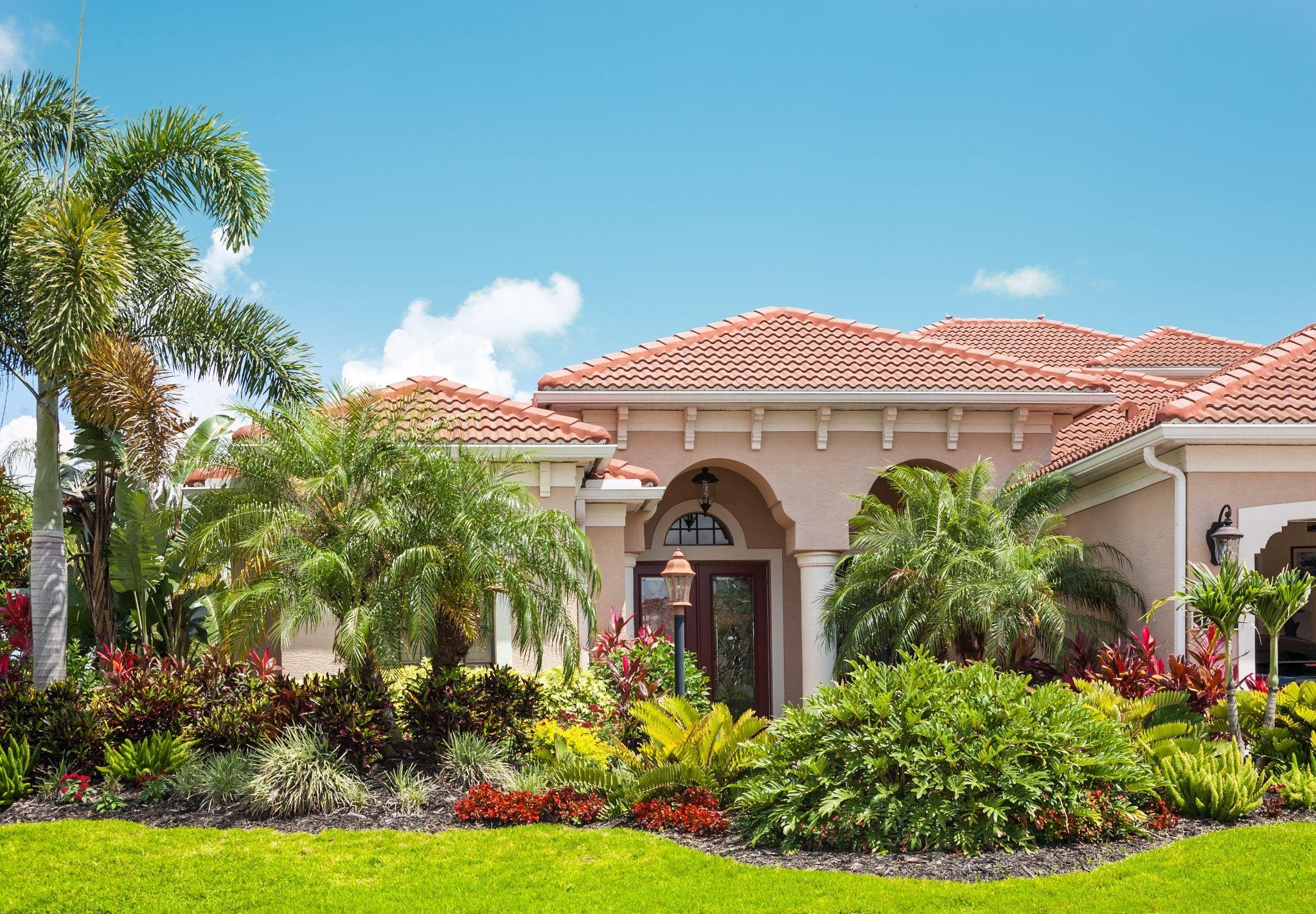 A beautiful house with a terracotta roof and colorful flower beds, accentuated by bright blue skies.