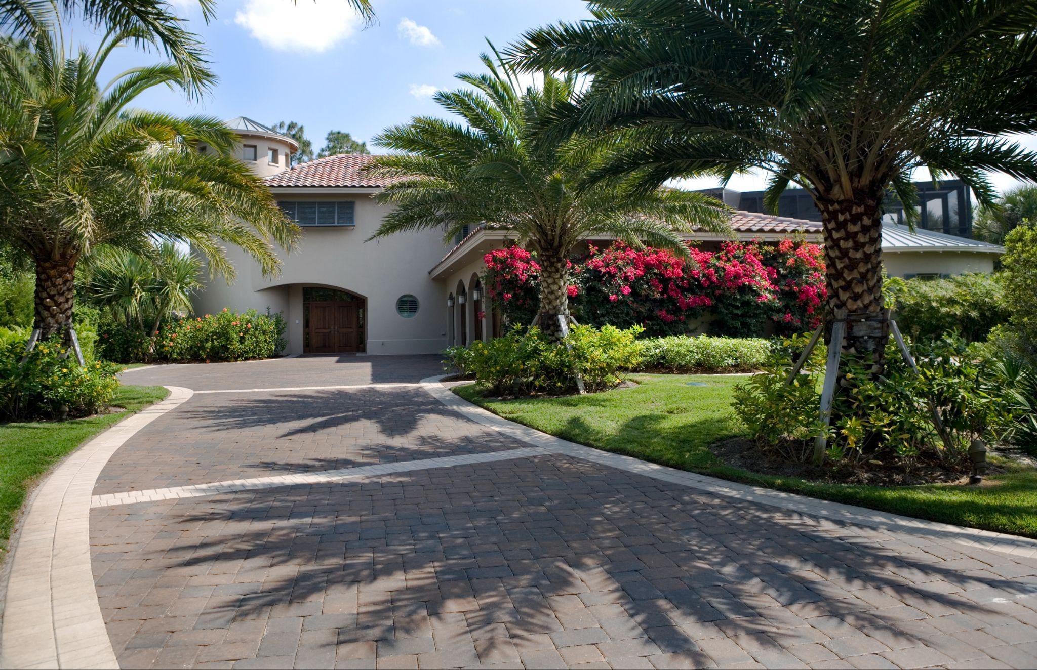 A scenic view of a residential area with colorful flowers and well-maintained sidewalks, flanked by palm trees and bright blue skies.