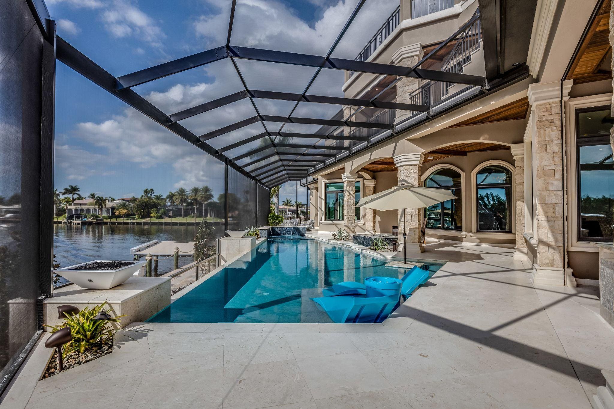 A stunning pool area with a modern design, featuring a clear blue pool and lounge chairs under a protective screen, overlooking a serene water view.