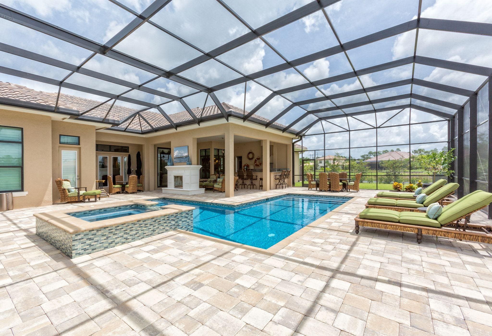 A stunning pool area with a modern design, featuring a clear blue pool and lounge chairs under a protective screen, overlooking a serene water view.