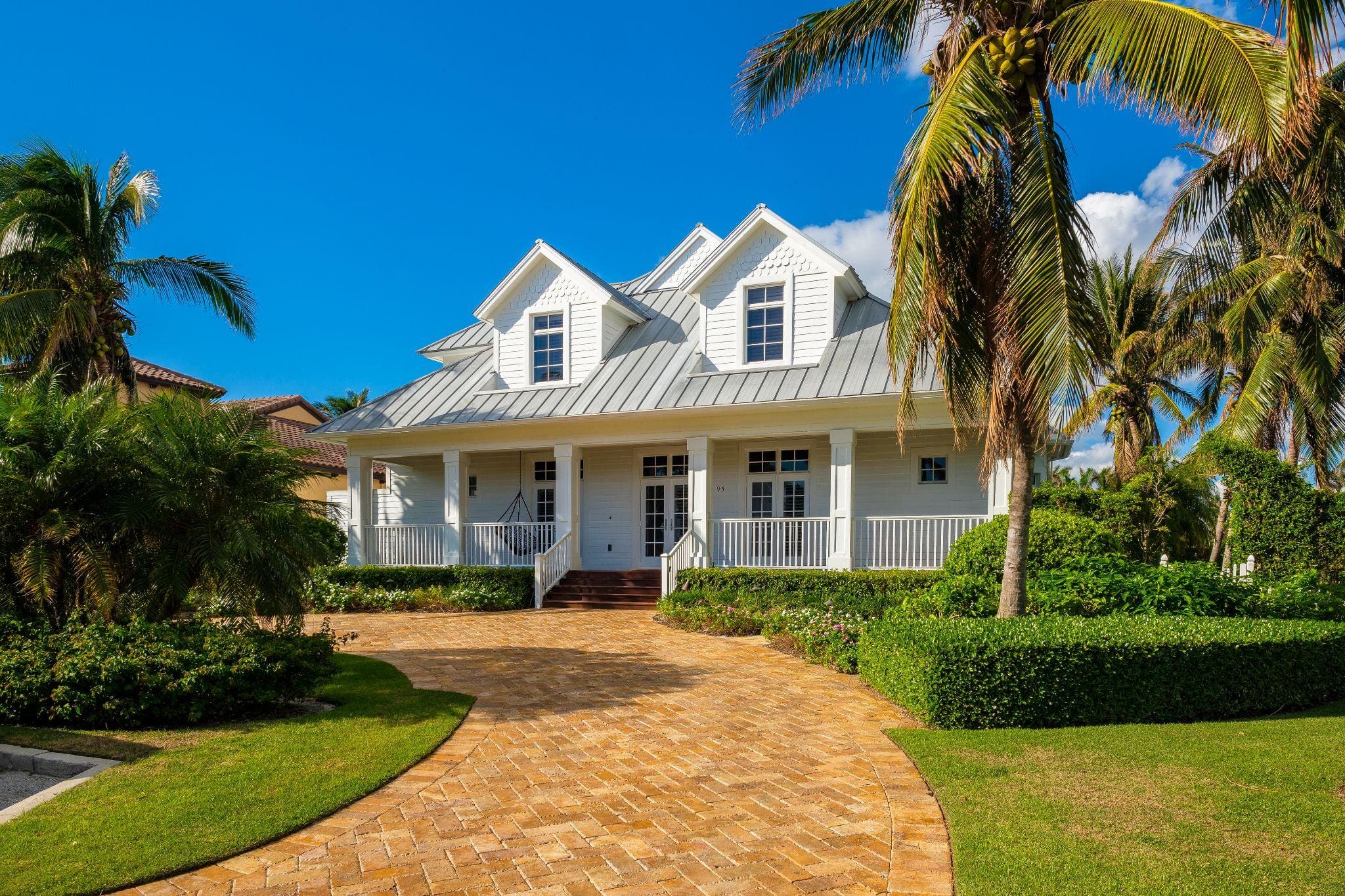 A vibrant pink house with a unique texture, surrounded by lush plants and palm trees, leading to a quaint pathway.