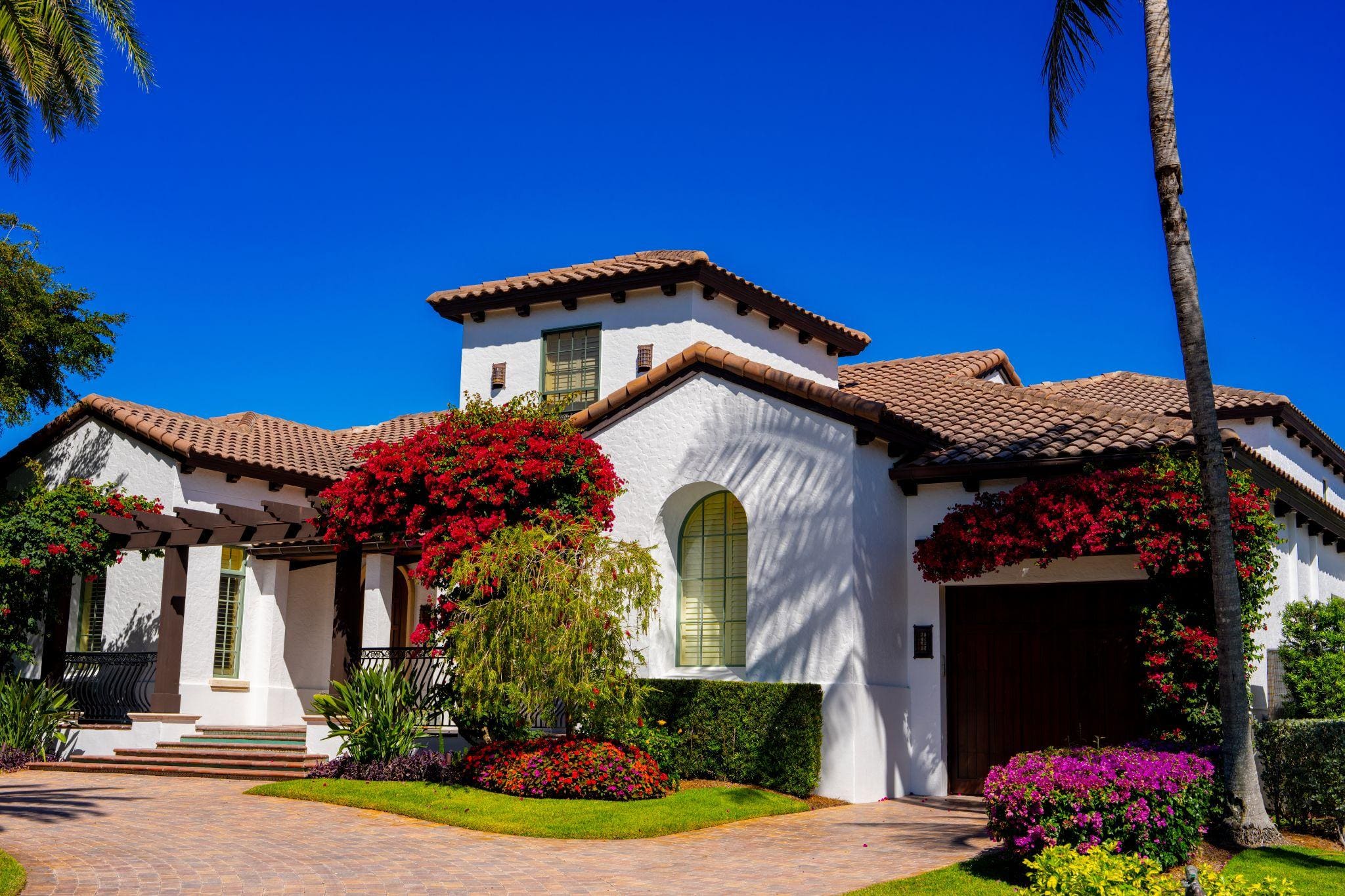 An elegant home with a Mediterranean style, surrounded by lush greenery and colorful flowers.