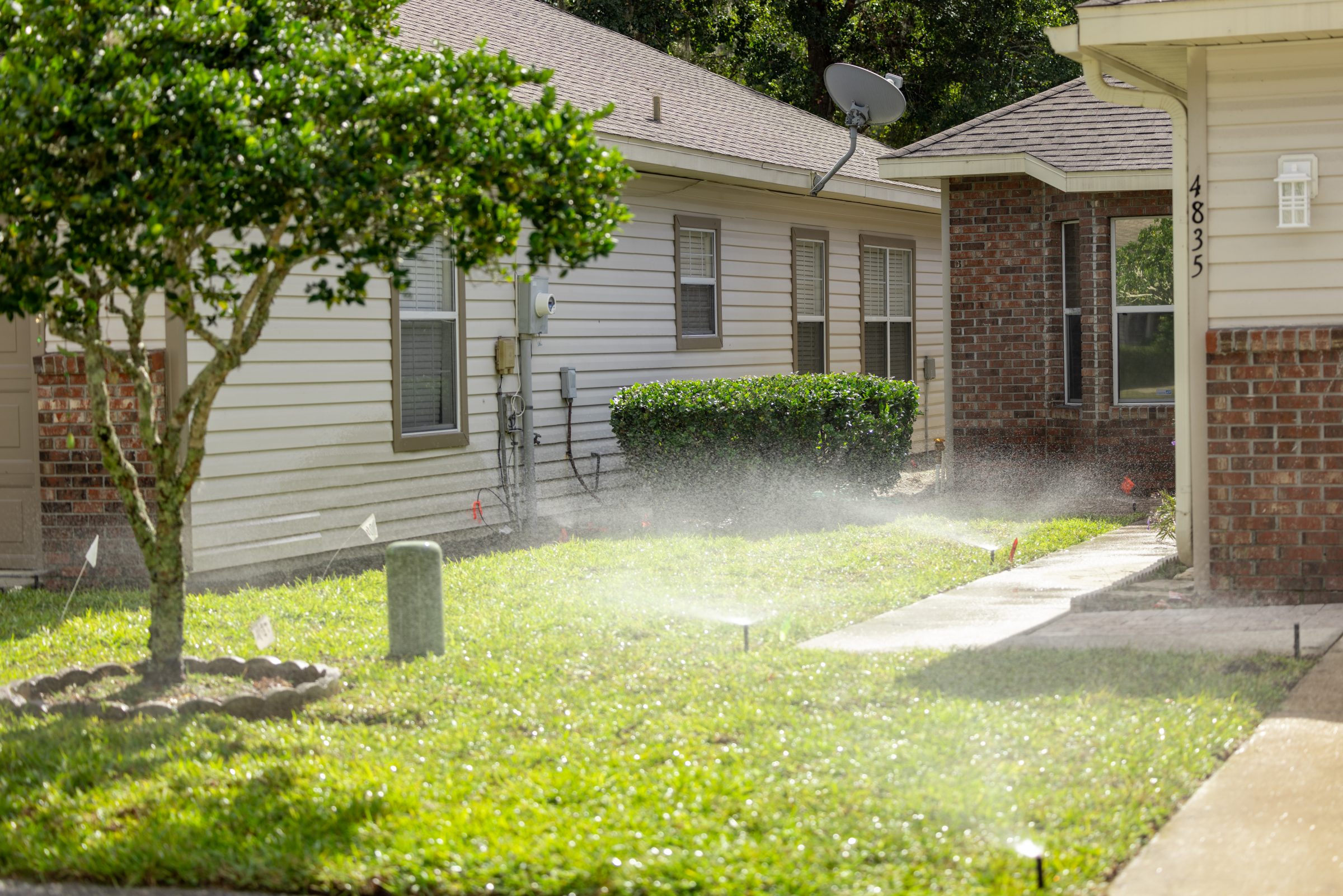 Sprinklers water lawn outside a suburban brick house