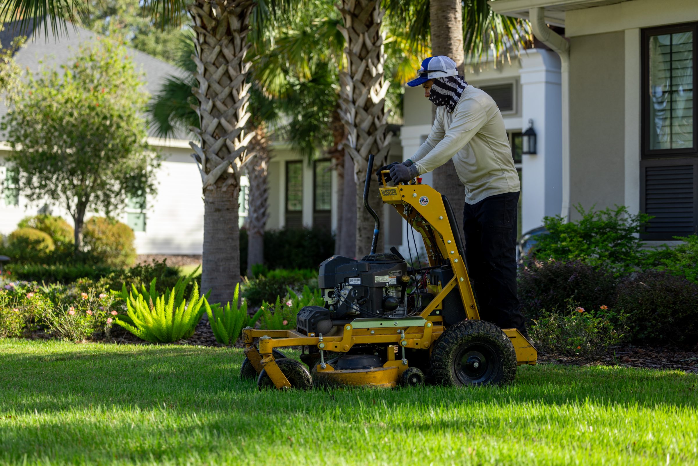 Landscaper mowing a residential lawn with a yellow mower