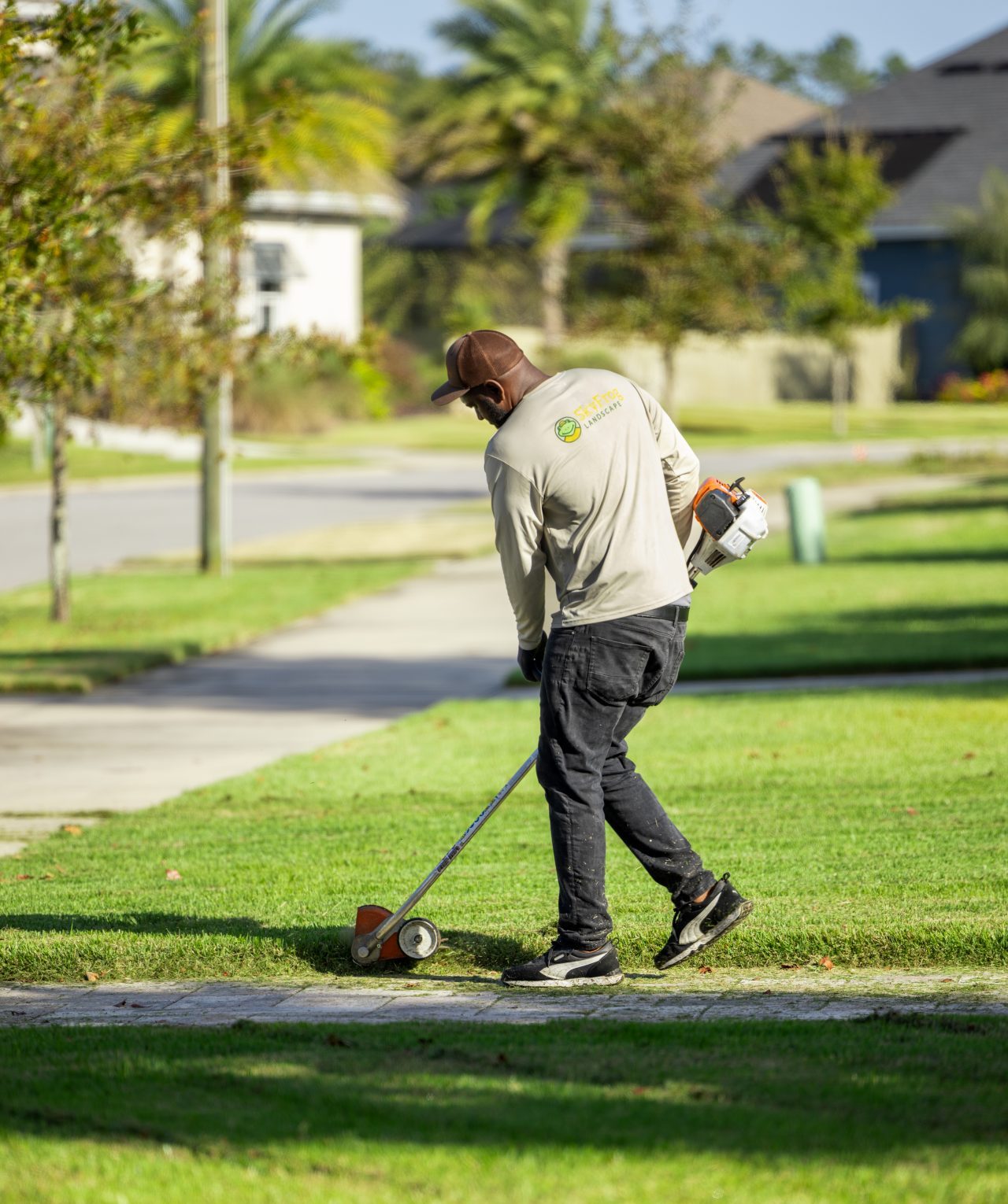 Landscaper edging a lawn beside a residential sidewalk