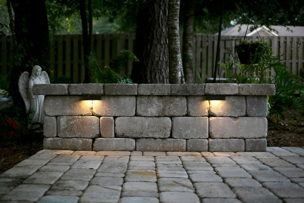 Illuminated stone garden wall beside angel statue