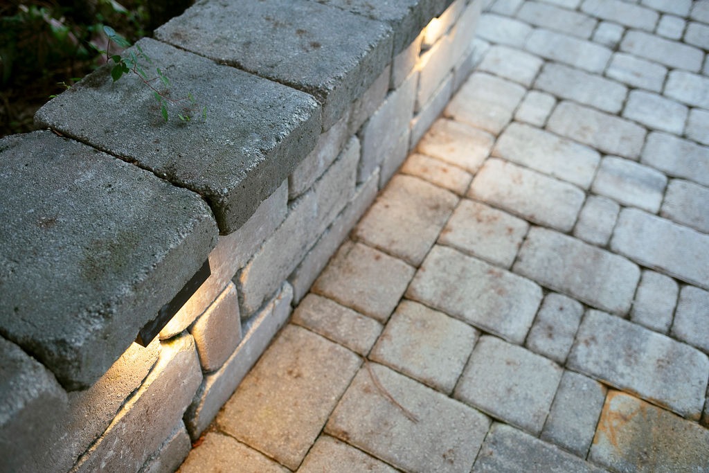 Stone retaining wall beside a lighted paver walkway