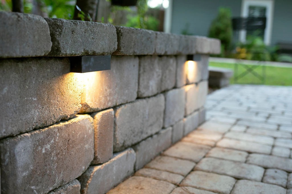 Warm lights illuminate a stone retaining wall beside patio