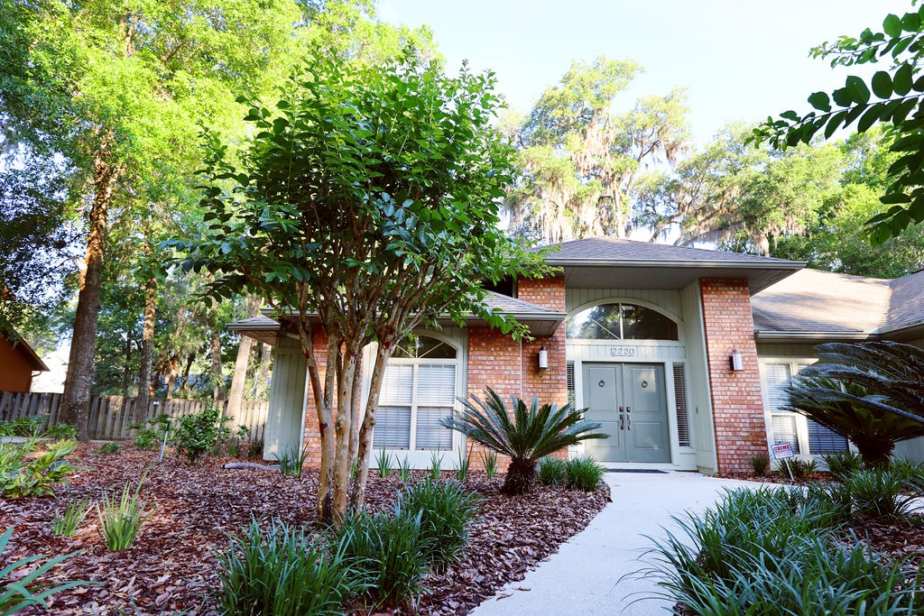 Brick suburban home entrance surrounded by lush landscaped trees