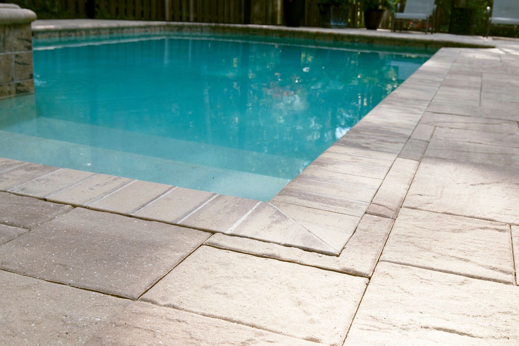 Turquoise backyard pool bordered by light stone pavers