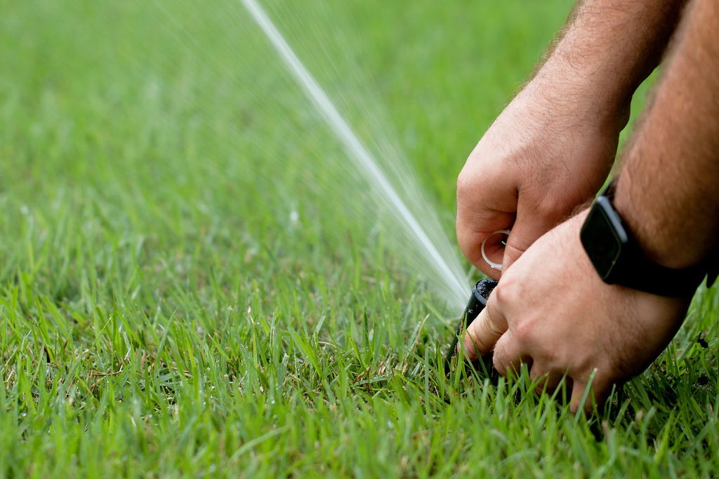 Person adjusting a lawn sprinkler spraying green grass