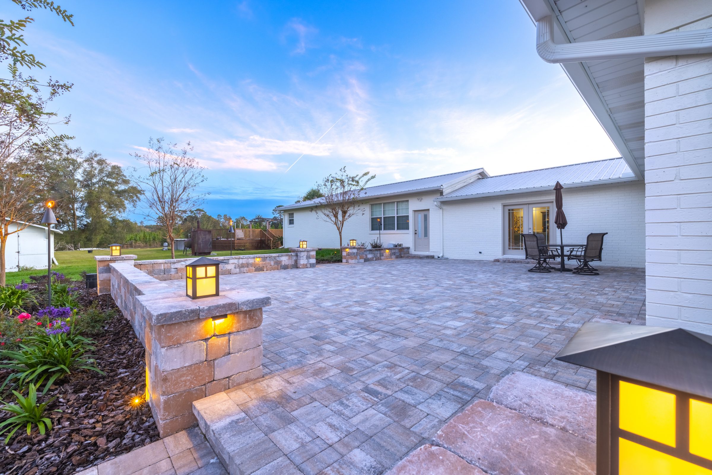 Illuminated stone patio beside white brick home at dusk