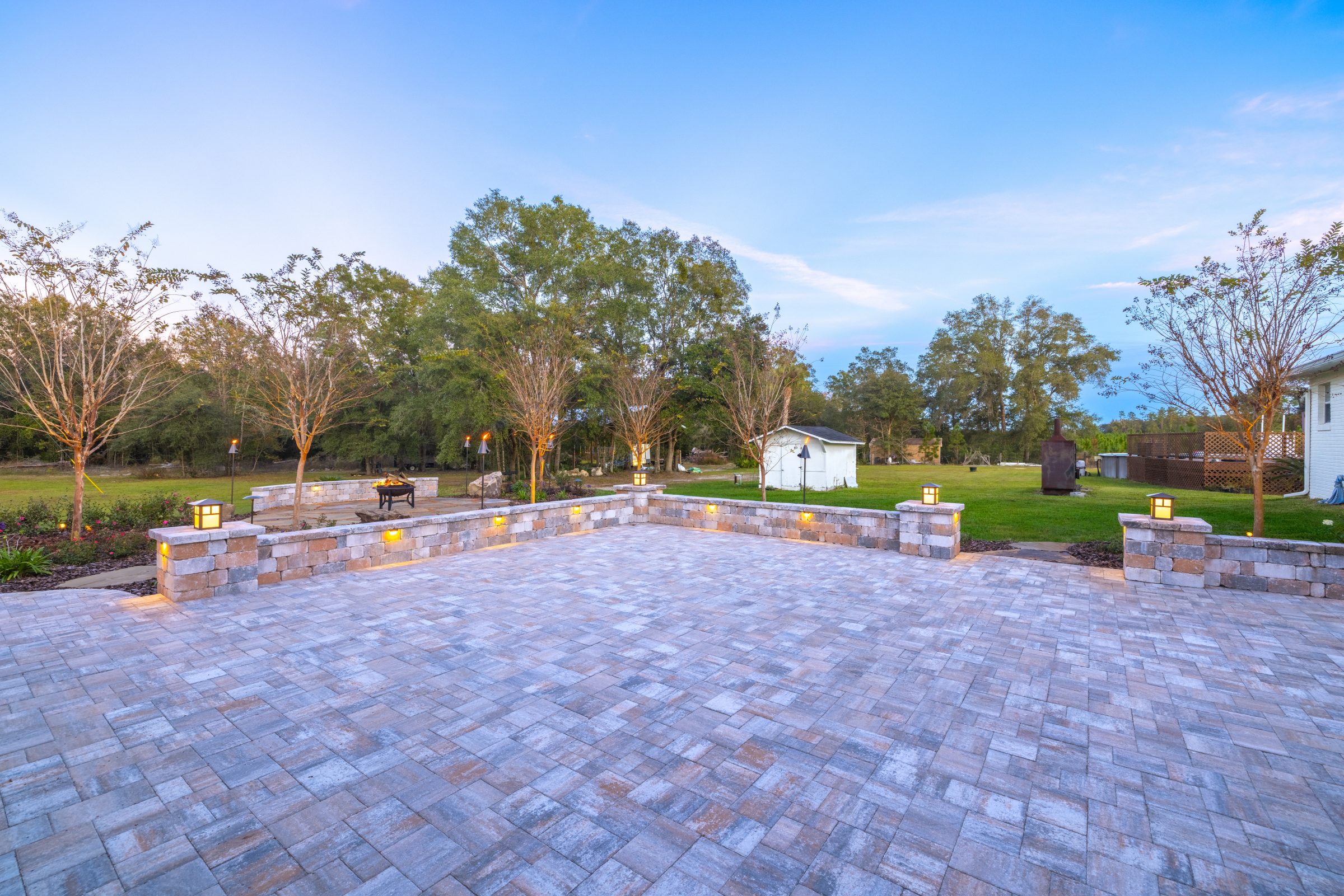 Illuminated stone patio and fire pit at dusk