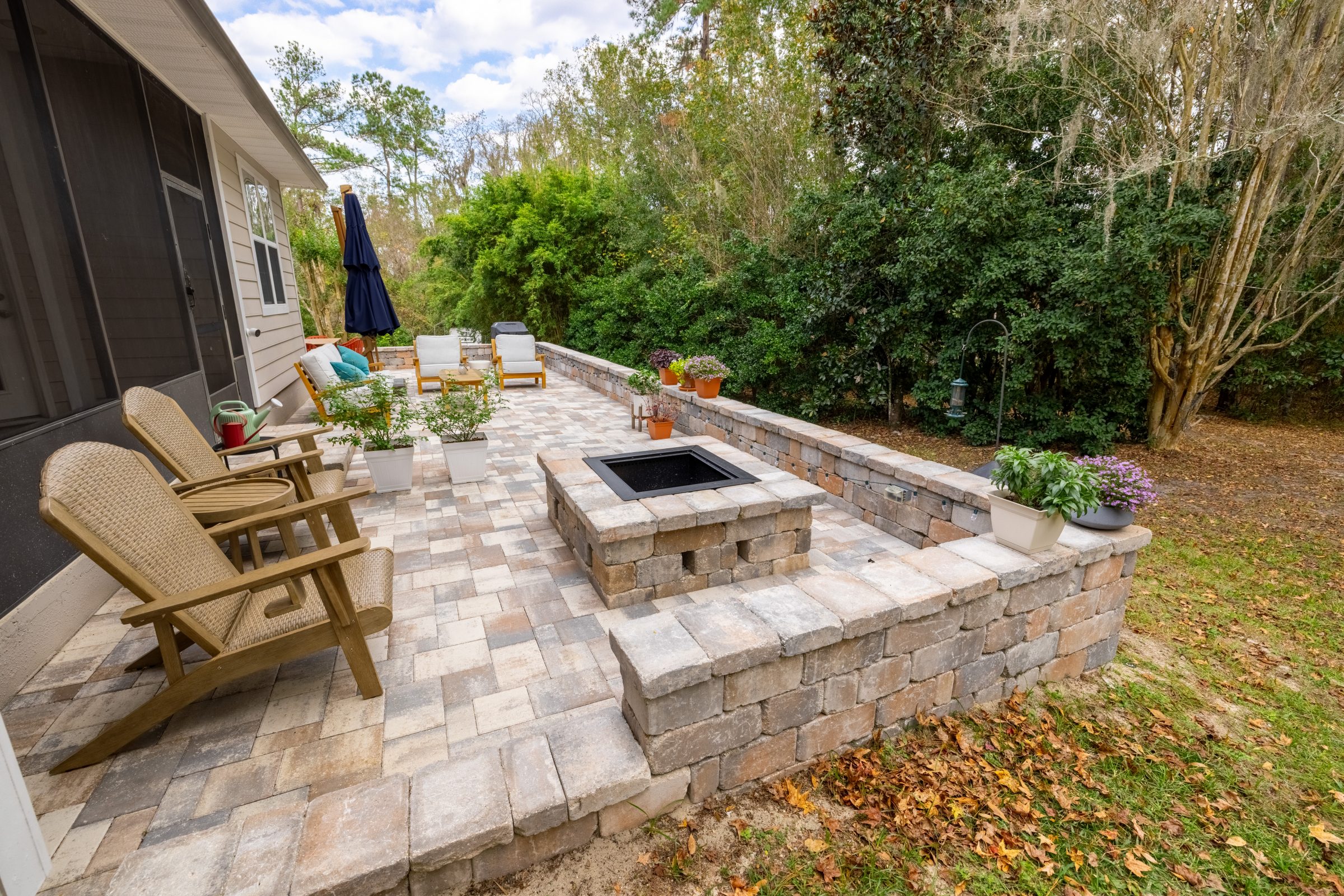 Paver patio with fire pit beside wooded backyard