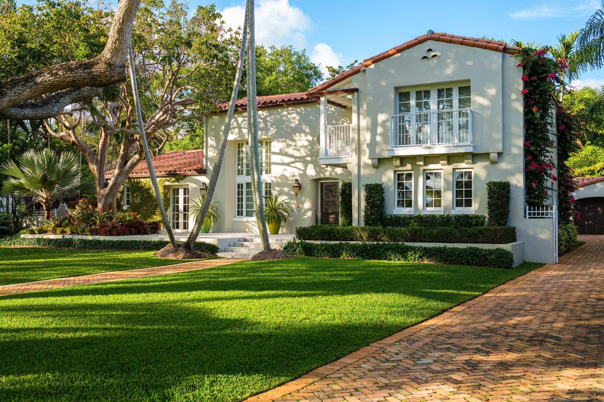 Mediterranean-style home with tropical landscaping and brick driveway