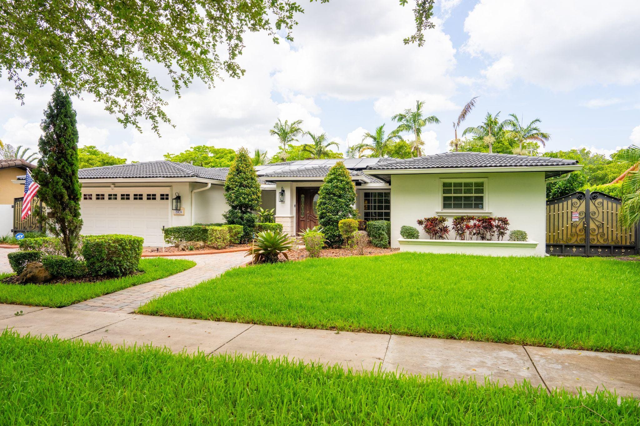Single-story home with lush lawn, palms, and garage