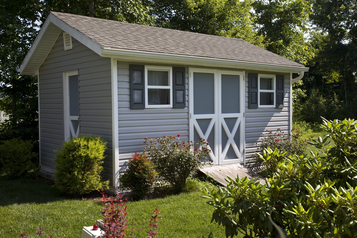 Gray garden shed with white doors and flowering shrubs