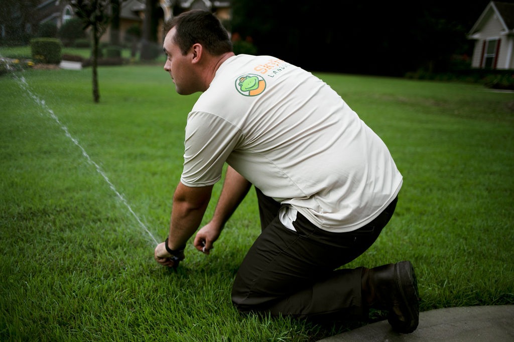 Lawn technician adjusting a sprinkler on green grass