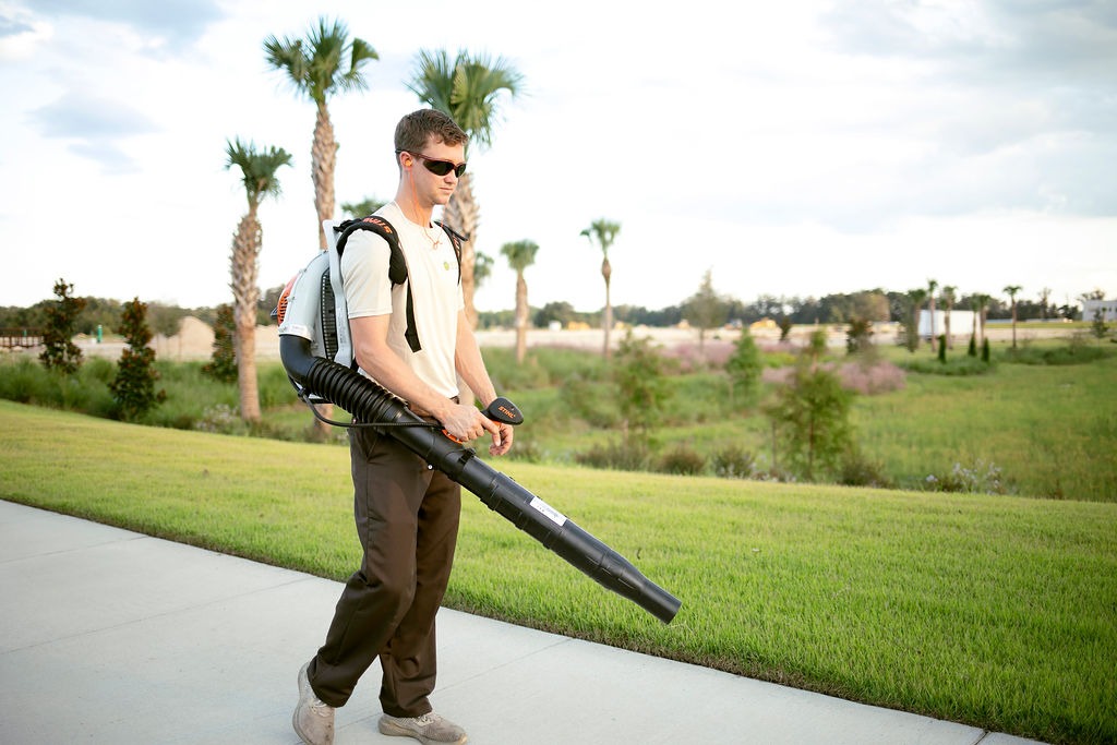 Man using backpack leaf blower beside landscaped lawn