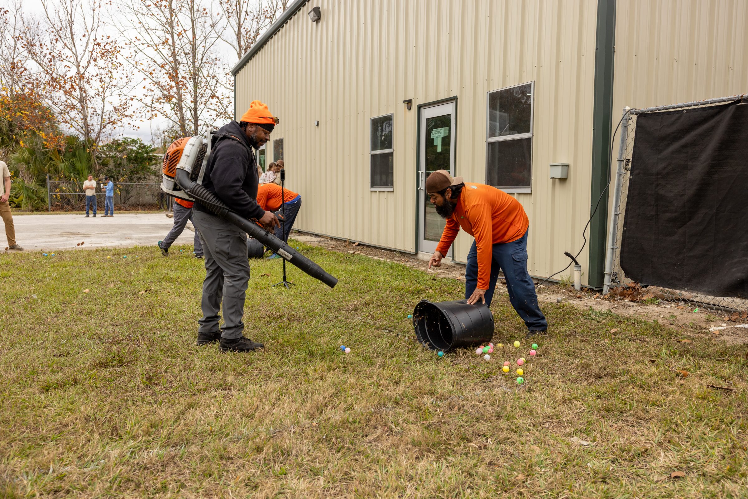 Volunteers use leaf blower near spilled colorful plastic eggs