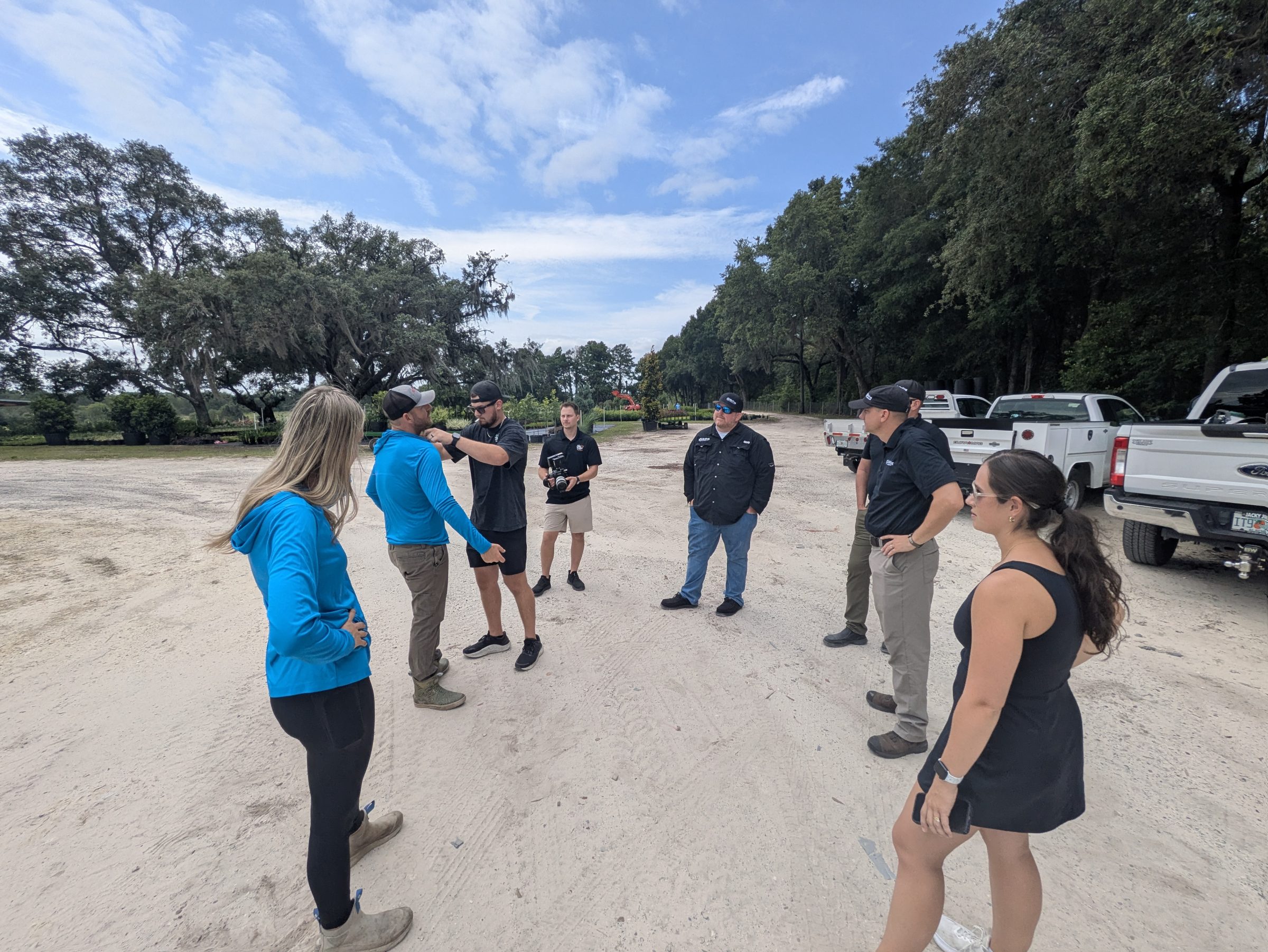 Group gathers beside pickup trucks under oak trees.
