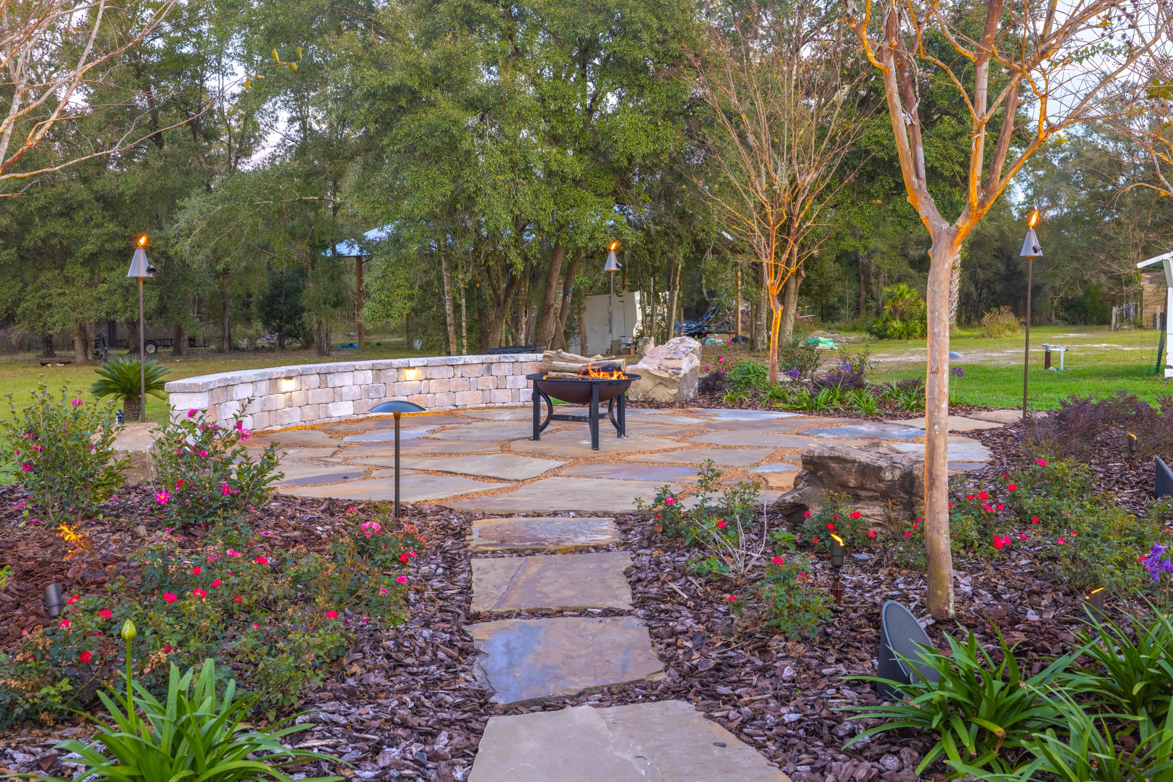 Garden patio with fire pit, flowers, and torch lights
